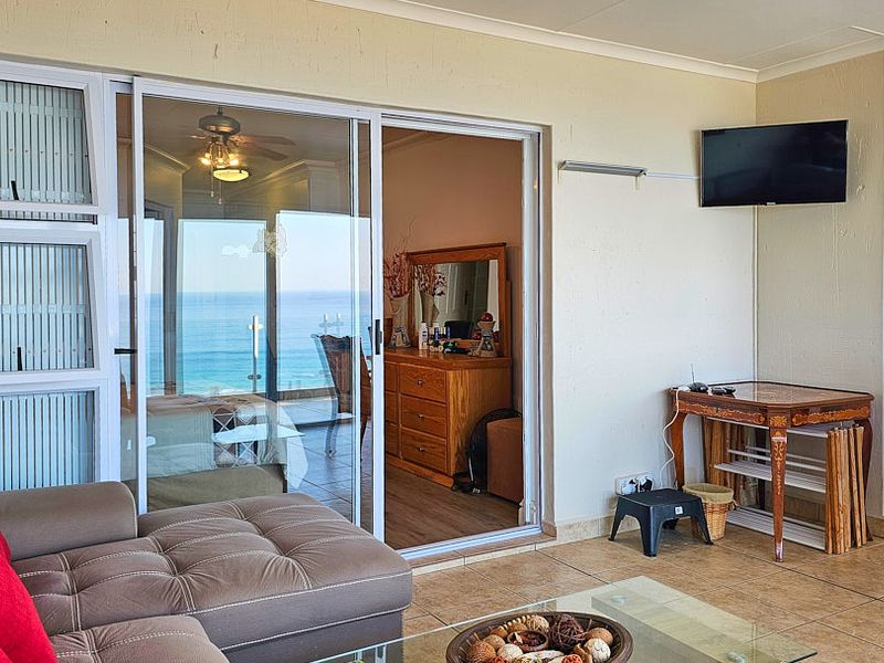 A covered balcony featuring tiled flooring, sliding glass doors, and a ceiling fan, offering a view of the ocean.