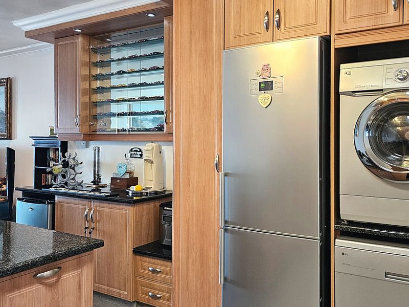 A well-appointed kitchen featuring warm wood cabinetry, granite countertops, recessed lighting, and integrated laundry appliances, offering a functional and cohesive living space.