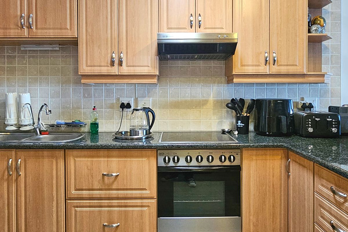 A functional kitchen featuring light wood-tone cabinetry, granite countertops, a tiled backsplash, and integrated stainless steel appliances including an oven and extractor fan.