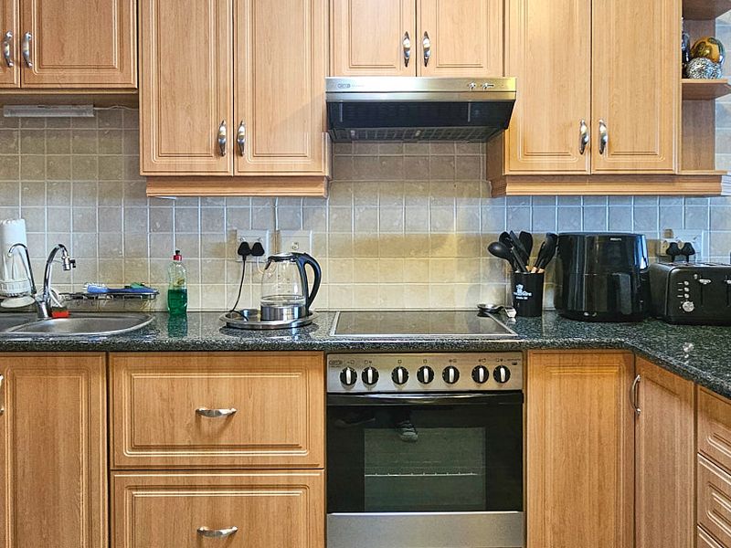 A functional kitchen featuring light wood-tone cabinetry, granite countertops, a tiled backsplash, and integrated stainless steel appliances including an oven and extractor fan.