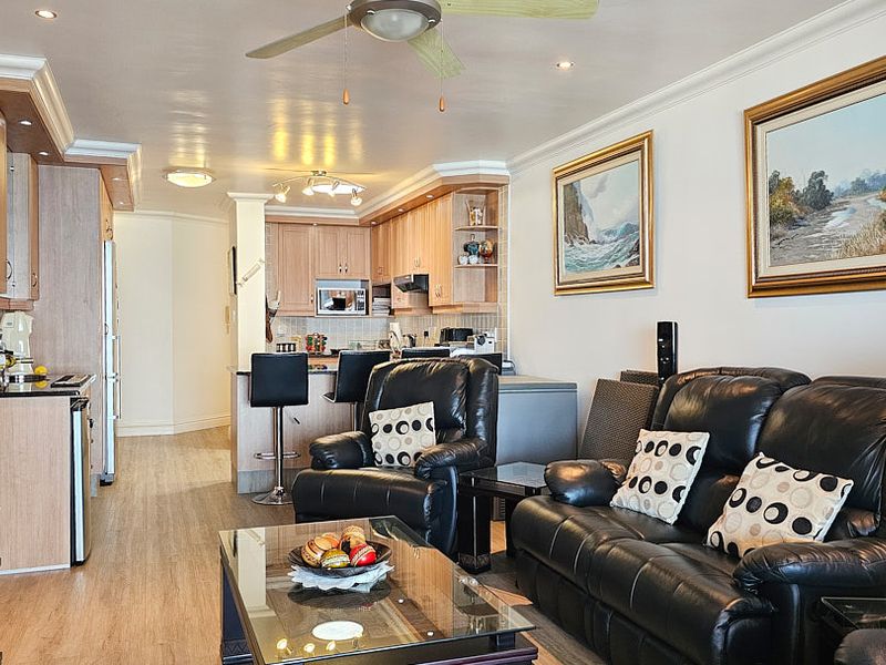 Open-plan living area featuring a functional kitchen with built-in cabinetry, breakfast counter, and laminate flooring throughout the combined space.