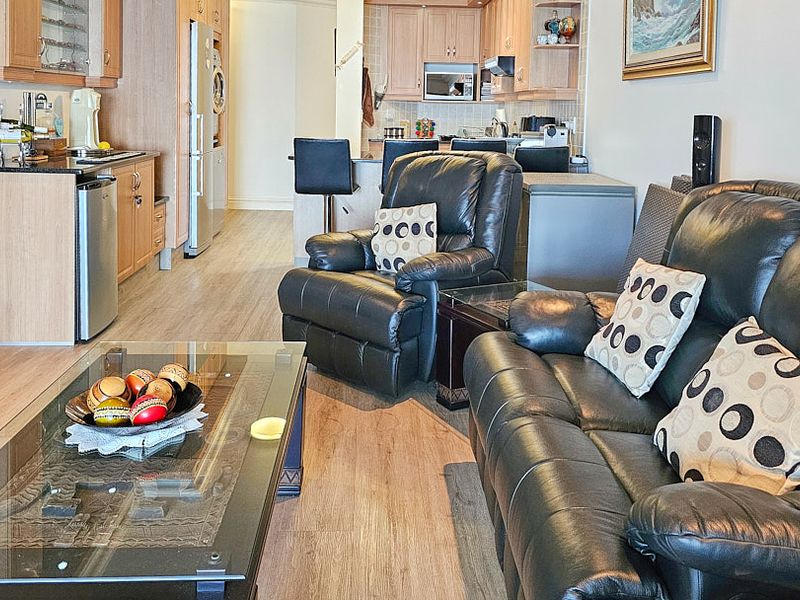 Open-plan living and kitchen area featuring light wood cabinetry, laminate flooring, and a functional breakfast bar layout.