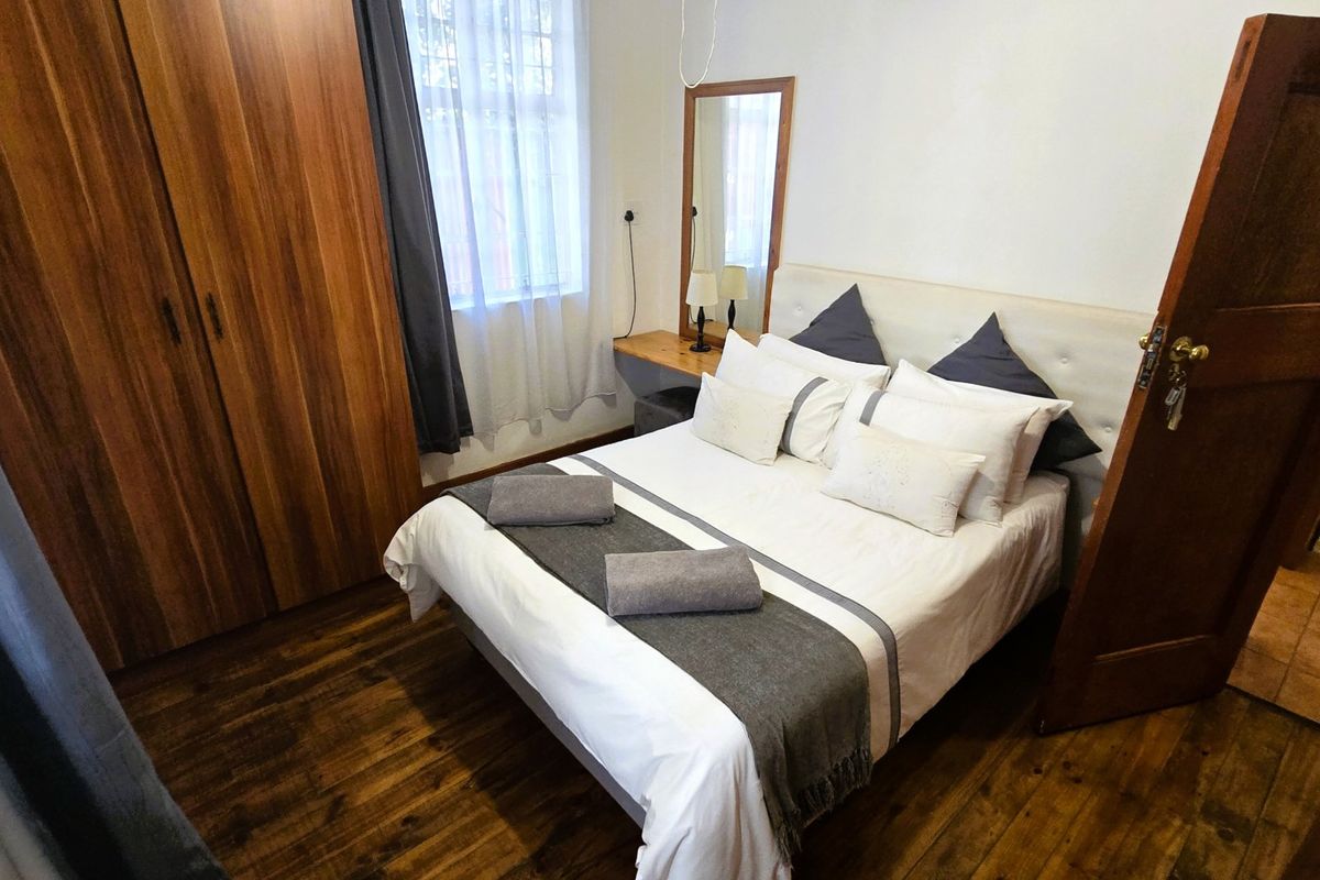 A well-maintained bedroom featuring warm wooden flooring, a built-in wardrobe, and a classic timber door.