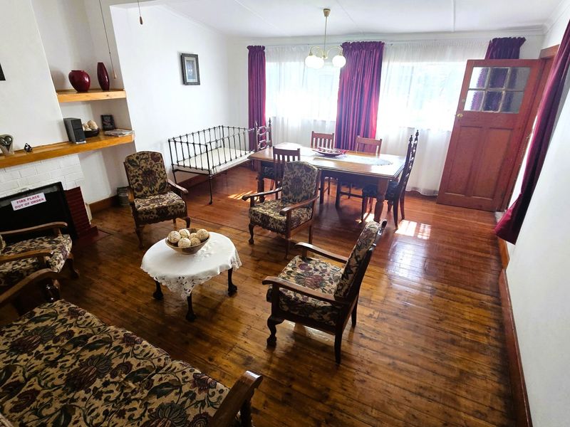 Open plan living and dining area featuring original hardwood flooring, a brick fireplace, and natural light through large windows.