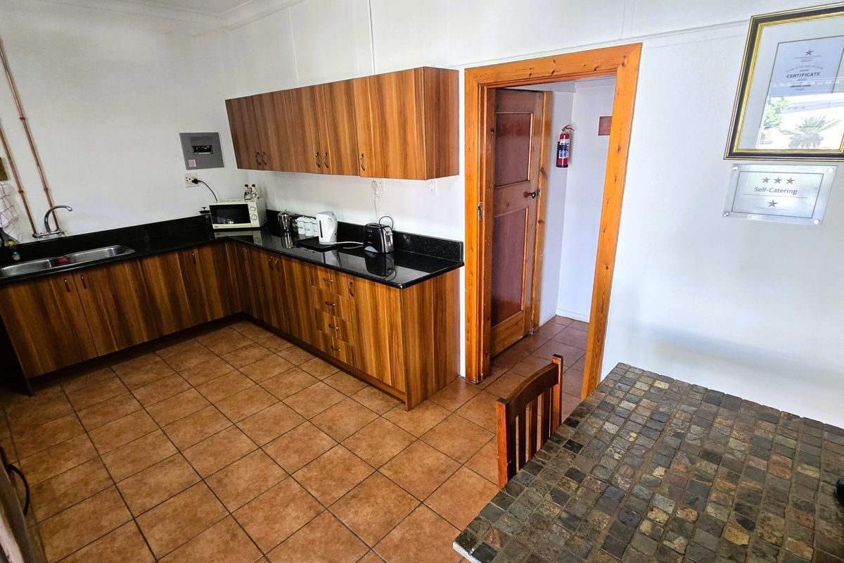 Functional kitchen featuring wood-look cabinetry, granite countertops, and tiled flooring, with direct access to an adjacent utility area.