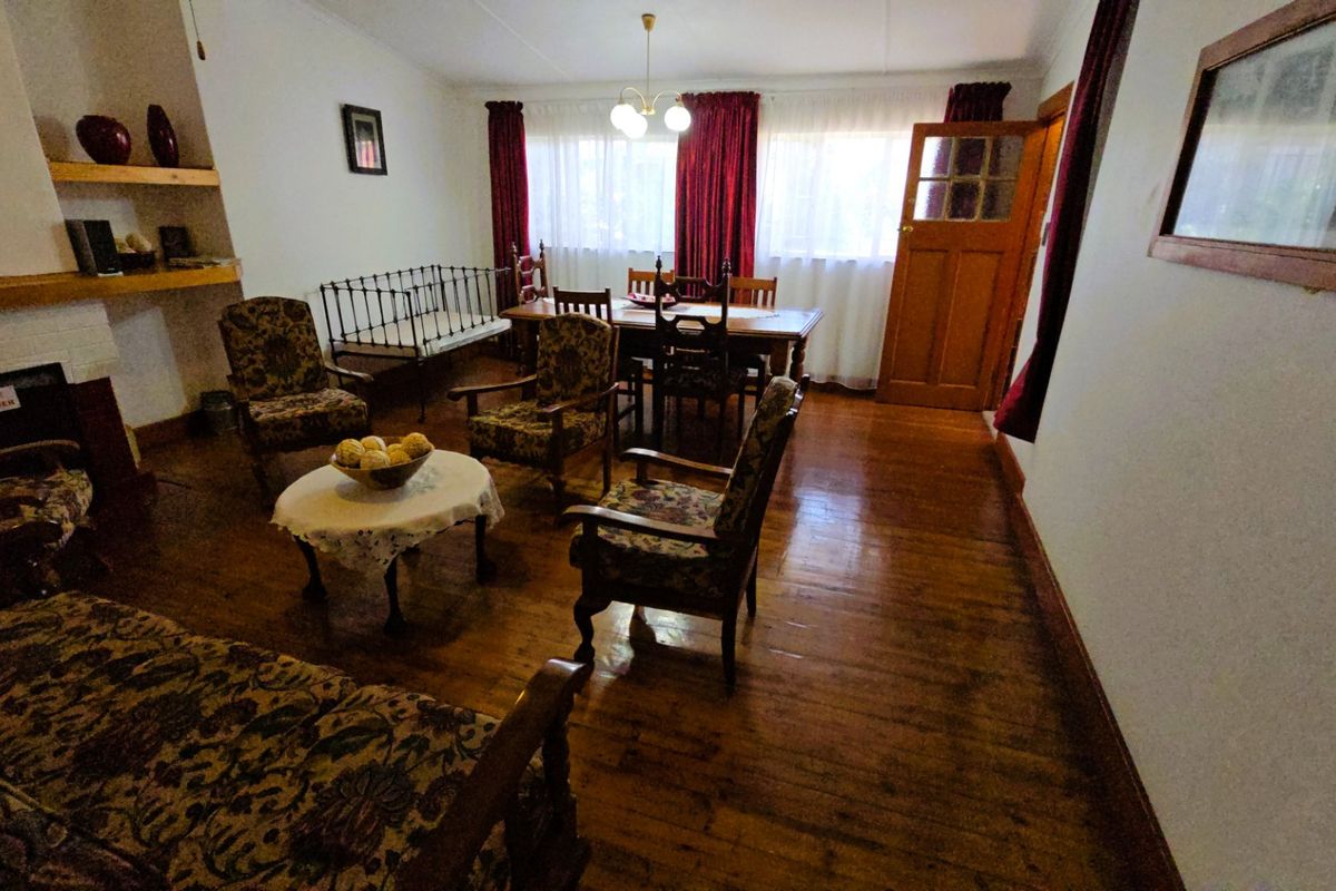 A living and dining area featuring original hardwood flooring, a fireplace, and a traditional timber door, offering a classic, dated aesthetic.