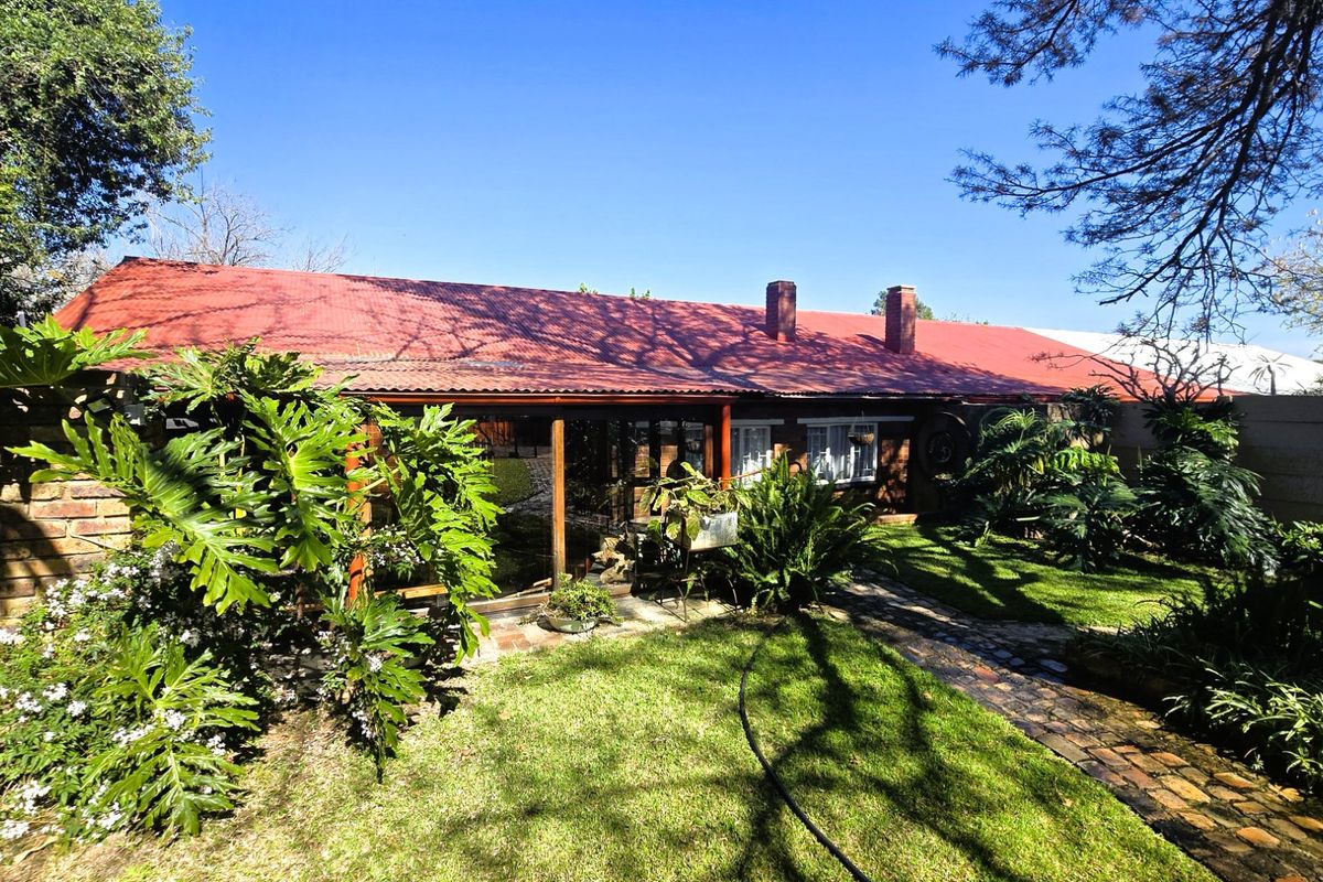 Rear view of the property featuring a red corrugated metal roof, brick chimney, and a covered patio area overlooking the garden.