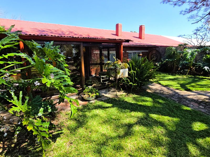 Rear view of the property featuring a corrugated metal roof, brick chimneys, and a well-maintained garden with a stone pathway.