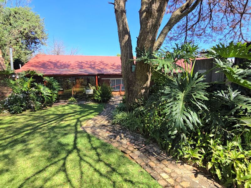 A view of the rear garden featuring a stone pathway leading to the house with a red metal roof and brick chimney.