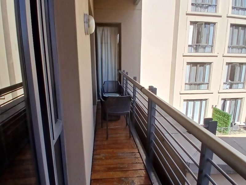 A narrow balcony featuring timber decking, metal railings, and a wall-mounted light fixture, overlooking the adjacent building facade.