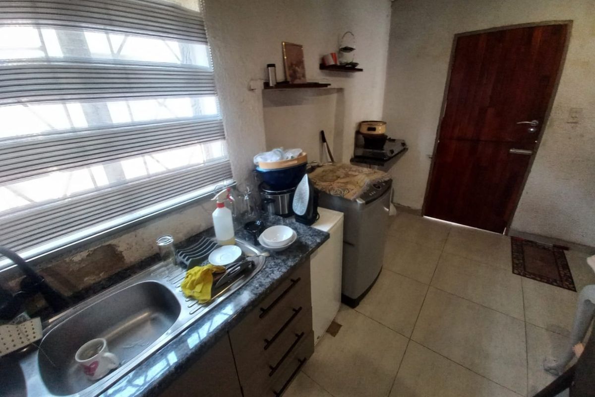 A compact kitchen area featuring a stainless steel sink, granite countertops, and tiled flooring, requiring some cosmetic updates to the wall finishes.