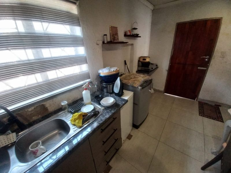 A compact kitchen area featuring a stainless steel sink, granite countertops, and tiled flooring, requiring some cosmetic updates to the wall finishes.