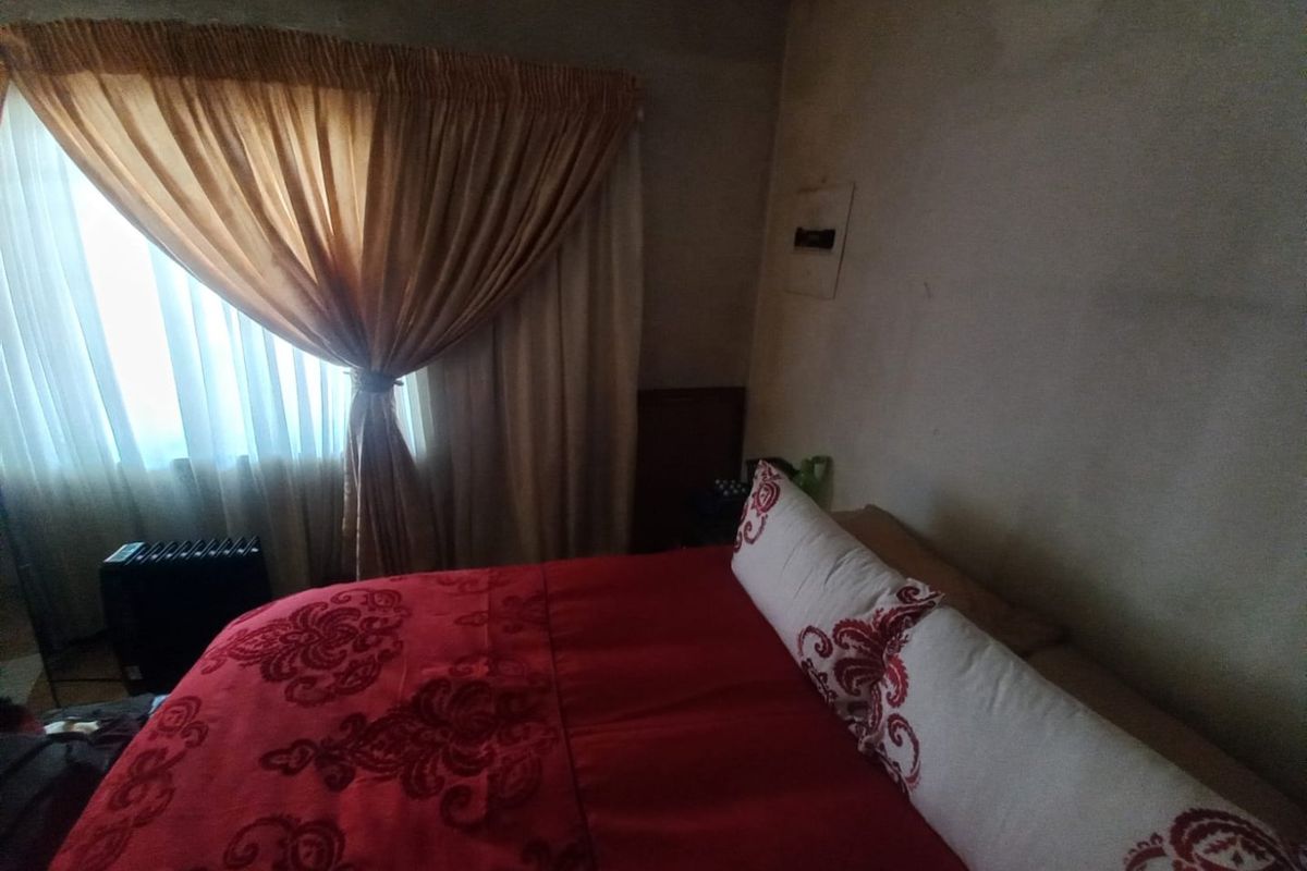 A bedroom featuring a window with curtains, showing signs of wall surface deterioration and staining requiring maintenance.
