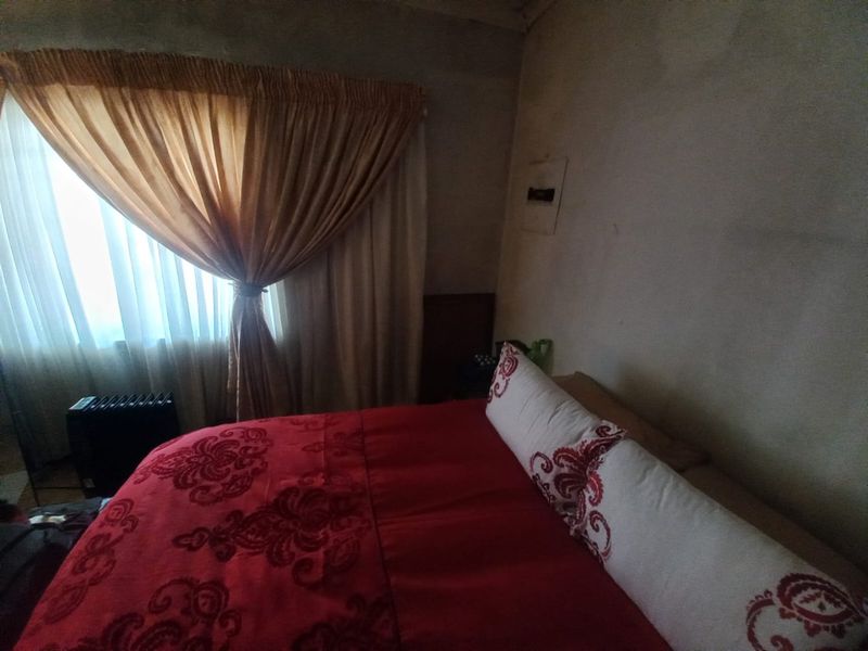 A bedroom featuring a window with curtains, showing signs of wall surface deterioration and staining requiring maintenance.