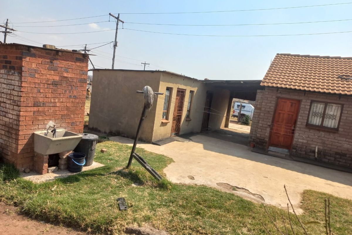Rear exterior view showing a concrete driveway, brick outbuilding, and a standalone concrete wash basin area.
