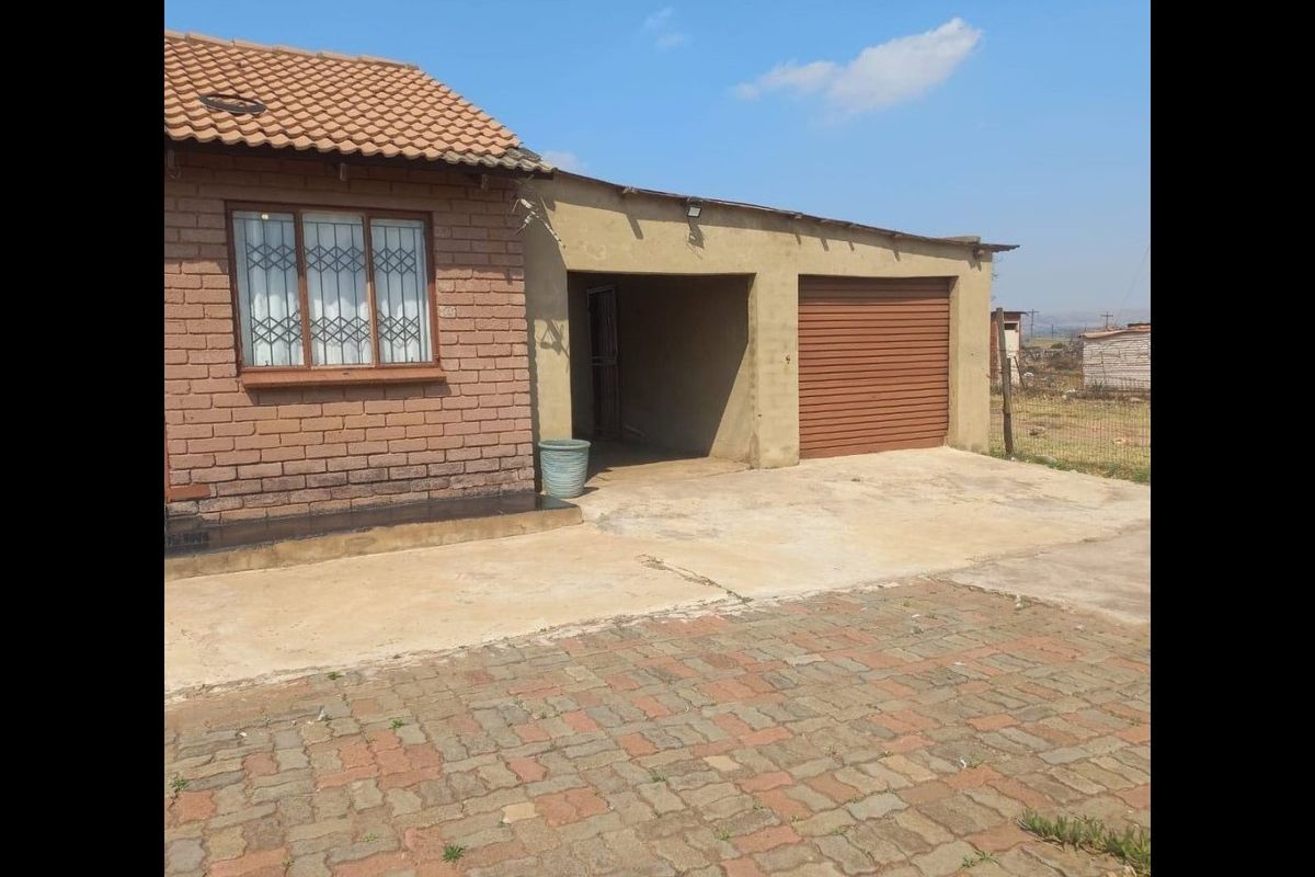 Front exterior view of a brick house featuring a tiled roof, security bars on windows, a single garage, and a paved driveway.