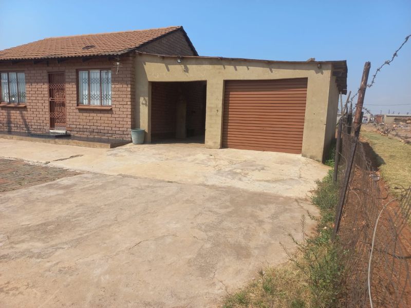 Front view of a single-story brick house featuring a tiled roof, security gates, and an attached garage with a concrete driveway.
