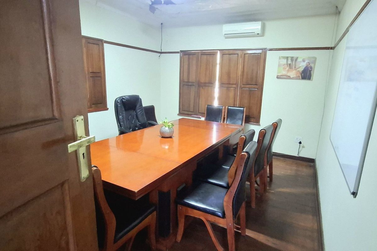 A functional office space featuring hardwood flooring, wooden window shutters, a wall-mounted whiteboard, and a split-system air conditioning unit.