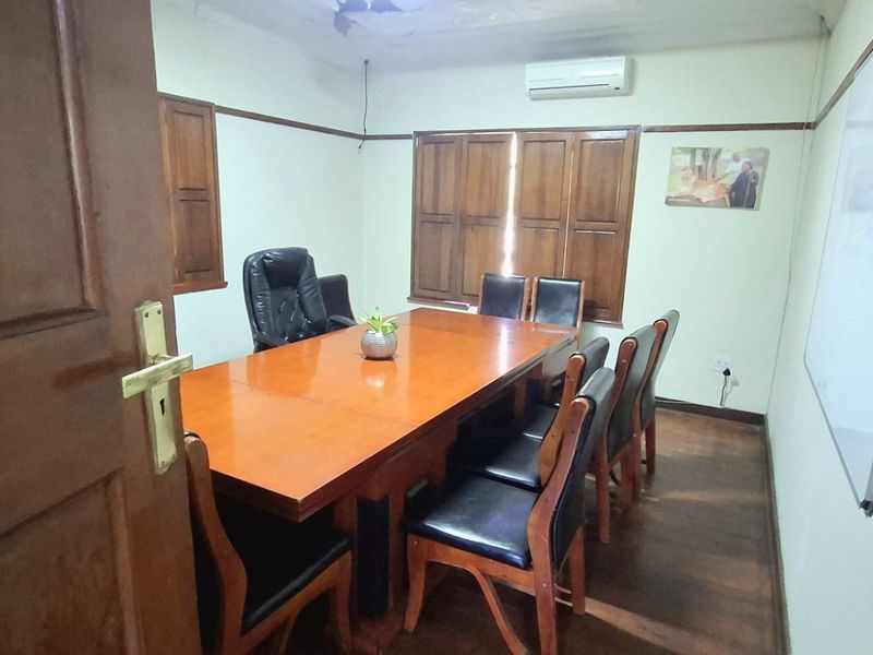 A functional office space featuring hardwood flooring, wooden window shutters, a wall-mounted whiteboard, and a split-system air conditioning unit.