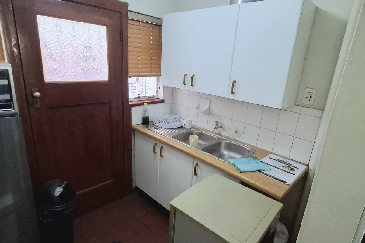 Compact scullery area featuring a double basin sink, tiled splashback, and built-in cabinetry with direct access to an exterior door.