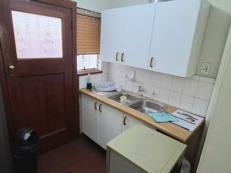 Compact scullery area featuring a double basin sink, tiled splashback, and built-in cabinetry with direct access to an exterior door.