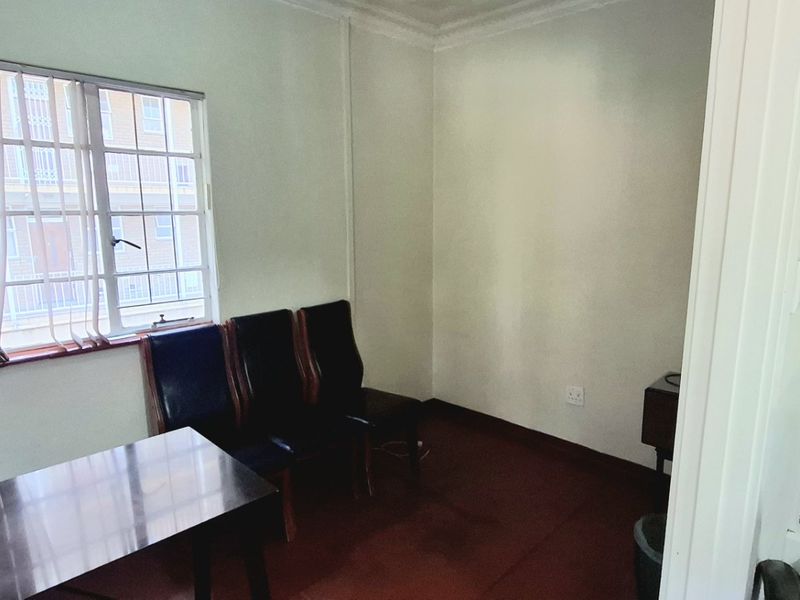 A functional office space featuring carpeted flooring, a large window providing natural light, and standard electrical infrastructure.