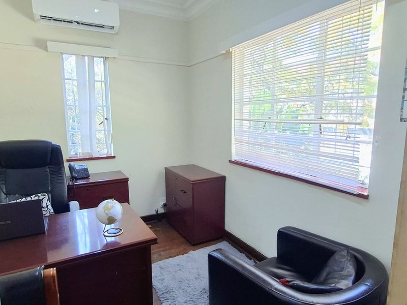 A functional office space featuring timber flooring, split-system air conditioning, and natural light through venetian blinds.