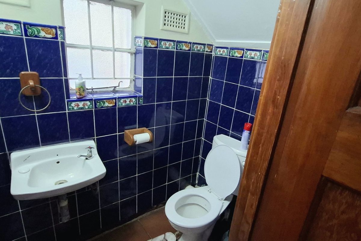 A compact bathroom featuring dark blue wall tiles with decorative accents, a wall-mounted basin, and a standard toilet.