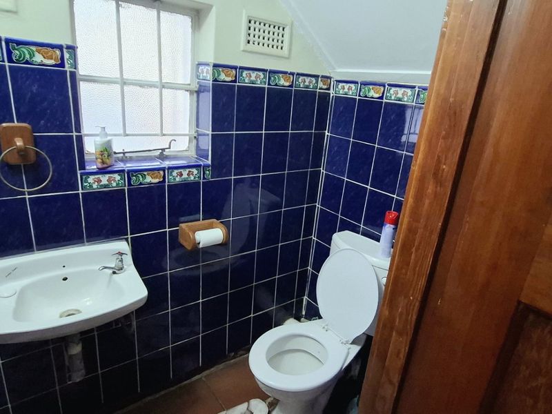 A compact bathroom featuring dark blue wall tiles with decorative accents, a wall-mounted basin, and a standard toilet.