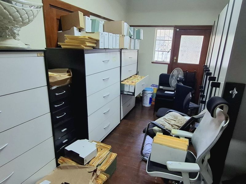A functional office space featuring parquet flooring and a secure exterior door, currently utilized for storage and administrative tasks.