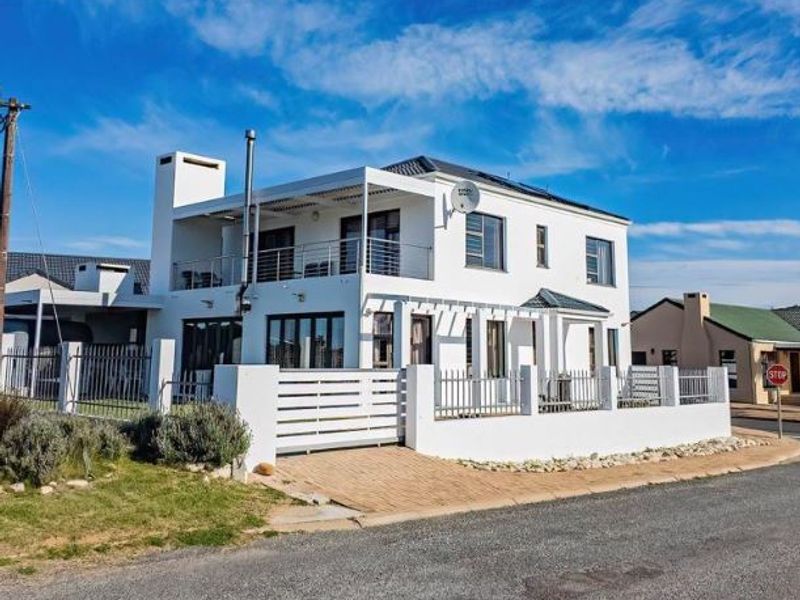 A well-maintained two-story residential property featuring a white facade, upper-level balcony, paved driveway, and secure perimeter fencing.