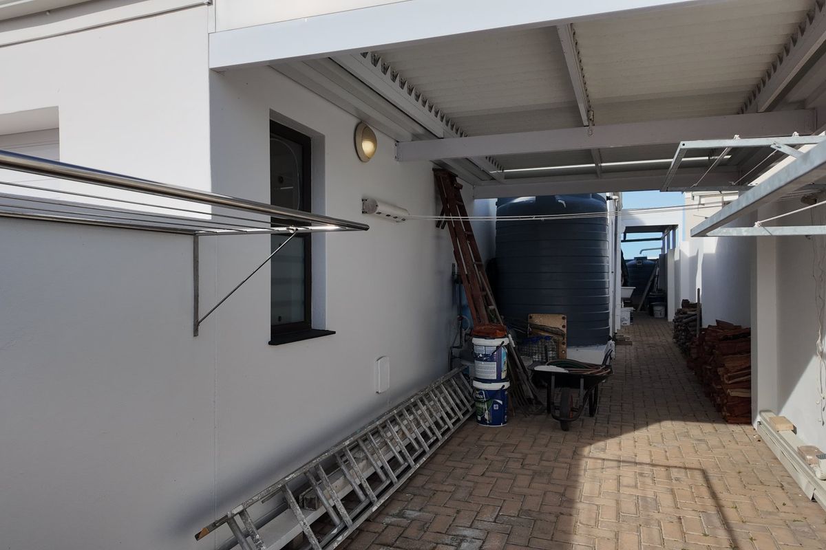 A paved rear utility area featuring a covered patio, wall-mounted clotheslines, and a large water storage tank.