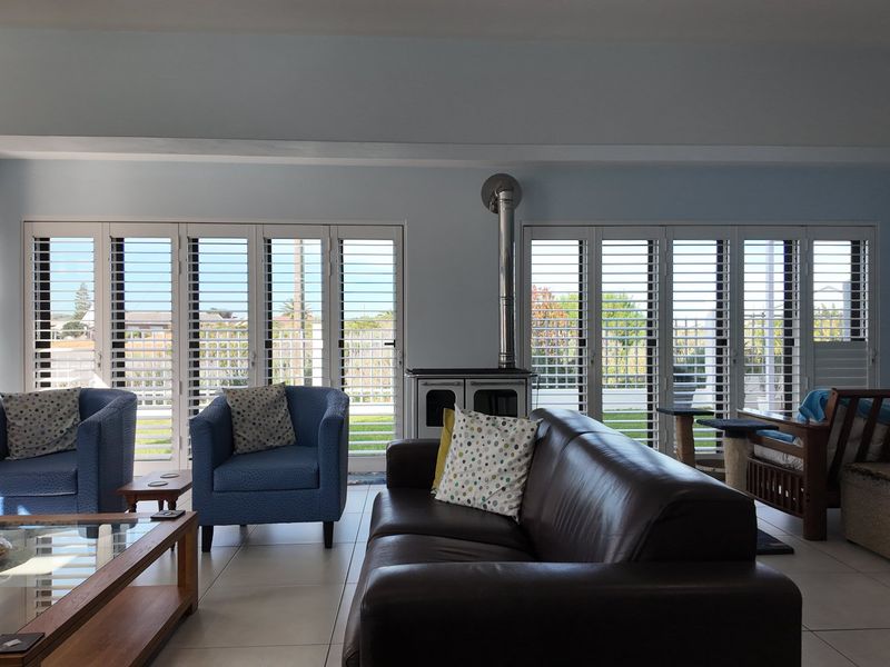 Spacious living room featuring tiled flooring, a central freestanding fireplace, and large sliding glass doors fitted with white plantation shutters.