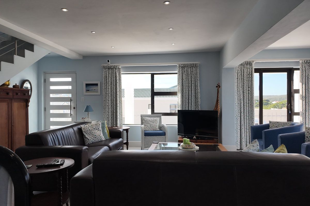 Spacious living room featuring recessed downlights, a modern staircase with metal railing, and large windows providing natural light and access to outdoor areas.