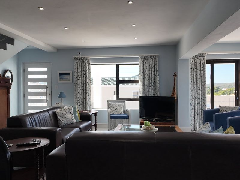 Spacious living room featuring recessed downlights, a modern staircase with metal railing, and large windows providing natural light and access to outdoor areas.