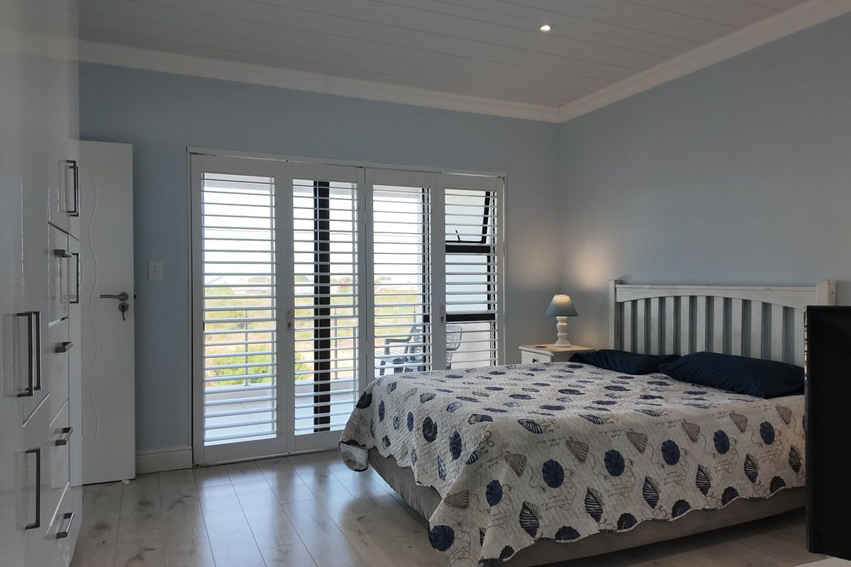 Spacious bedroom featuring light laminate flooring, built-in cupboards, and white plantation shutters opening onto a balcony with natural light.