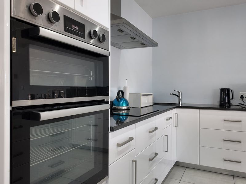 Modern kitchen featuring white high-gloss cabinetry, stone countertops, built-in double oven, and stainless steel extractor fan.