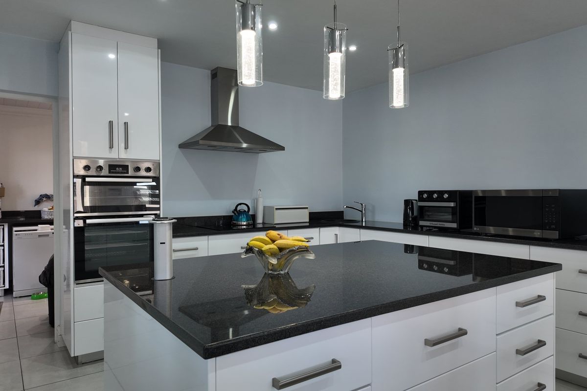 Modern kitchen featuring a central island with granite countertops, high-gloss white cabinetry, built-in oven, and contemporary pendant lighting.