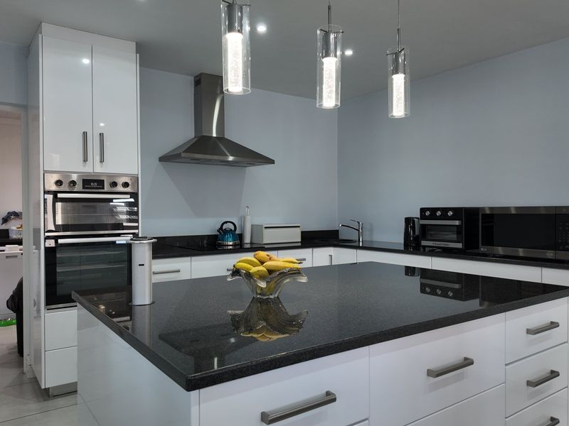 Modern kitchen featuring a central island with granite countertops, high-gloss white cabinetry, built-in oven, and contemporary pendant lighting.