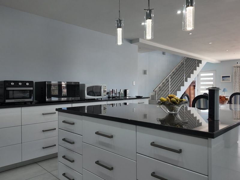 Modern open-plan kitchen featuring a central island with granite countertops, sleek white cabinetry, and contemporary pendant lighting, seamlessly flowing into the living area.