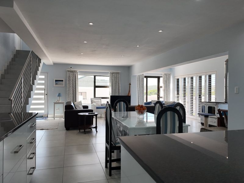 Spacious open-plan living and dining area featuring modern tiled floors, recessed lighting, a sleek kitchen, and a staircase leading to the upper level.