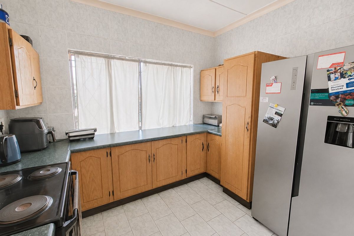 A functional kitchen featuring wood-finish cabinetry, laminate countertops, tiled backsplash, and tiled flooring, providing a practical workspace with integrated stove.