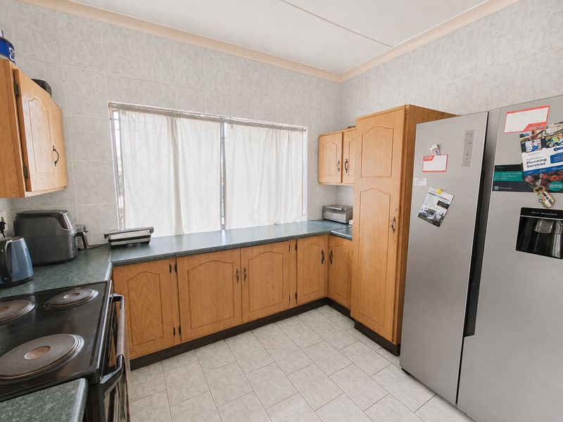 A functional kitchen featuring wood-finish cabinetry, laminate countertops, tiled backsplash, and tiled flooring, providing a practical workspace with integrated stove.