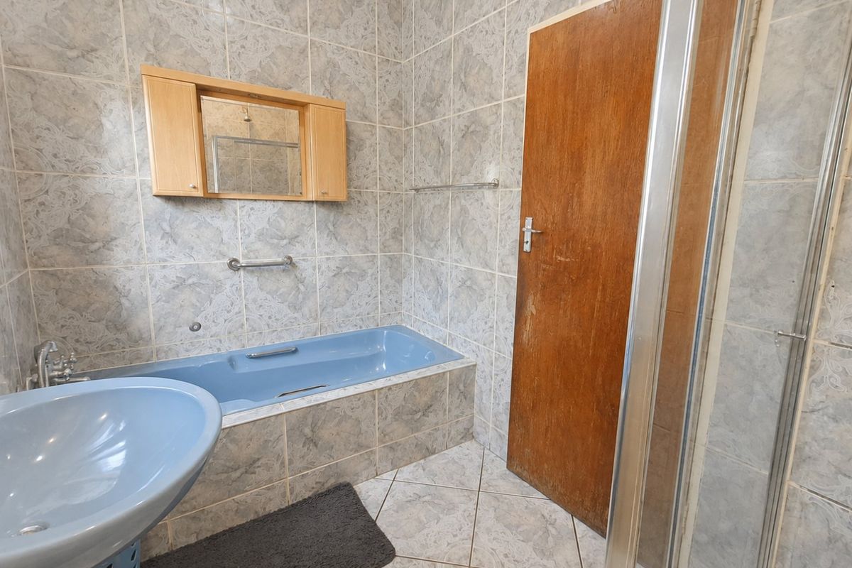 A dated bathroom featuring blue sanitaryware, a built-in bathtub, a separate shower enclosure, and full-height wall tiling.