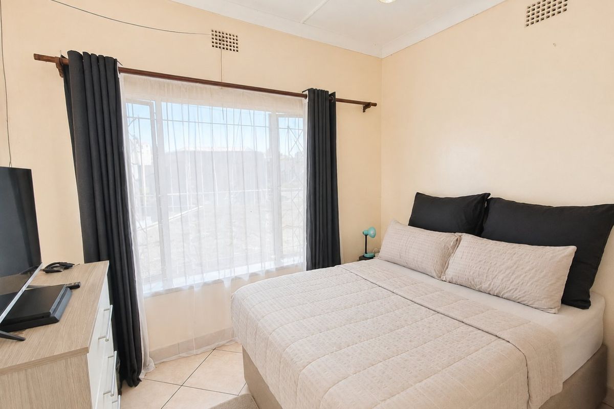 A functional bedroom featuring tiled flooring, security bars on the window, and integrated ceiling ventilation.