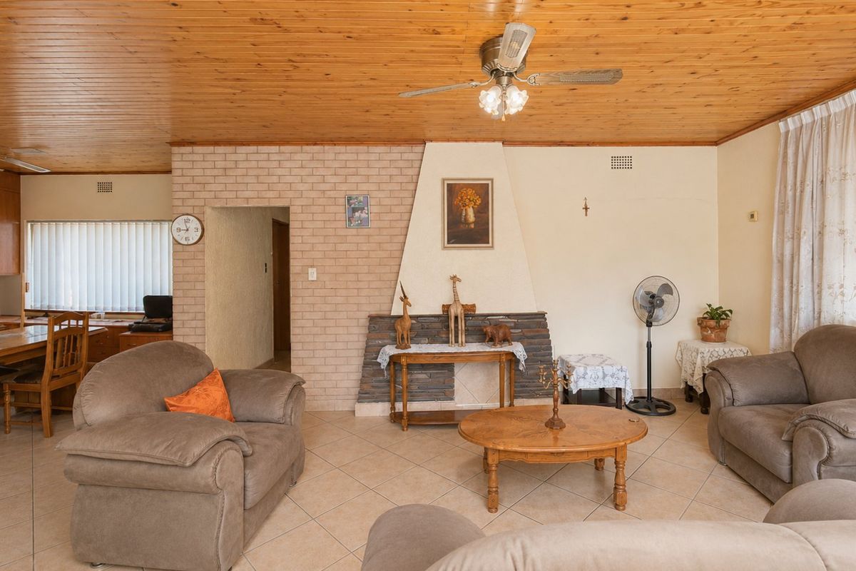 A living room featuring a distinctive timber tongue and groove ceiling, tiled flooring, and a central brick fireplace.