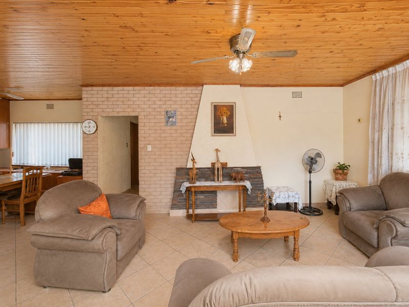 A living room featuring a distinctive timber tongue and groove ceiling, tiled flooring, and a central brick fireplace.