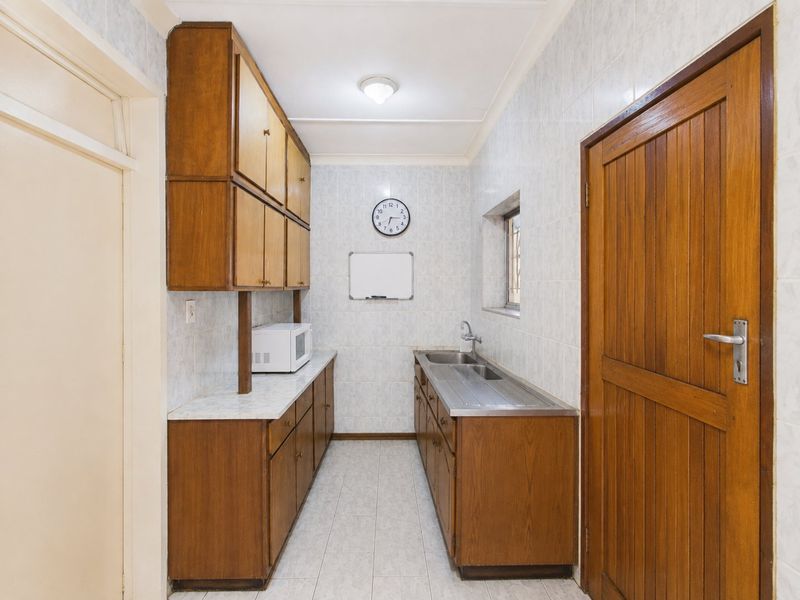 A functional scullery featuring built-in wooden cabinetry, laminate countertops, a stainless steel sink, and full-height wall tiling.