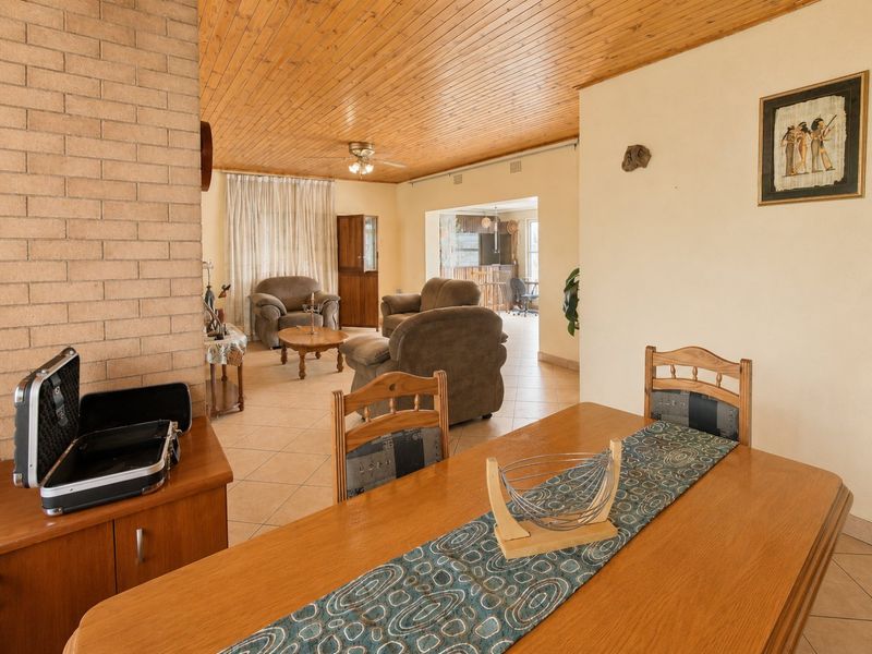 Open plan living and dining area featuring a brick fireplace, timber ceiling, and tiled flooring, offering a spacious layout with potential for modern updates.