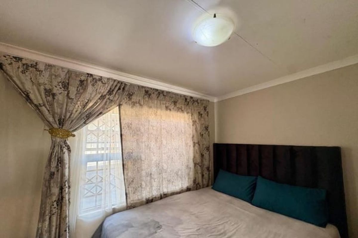 A bedroom featuring a window with security bars and a central ceiling light fixture.
